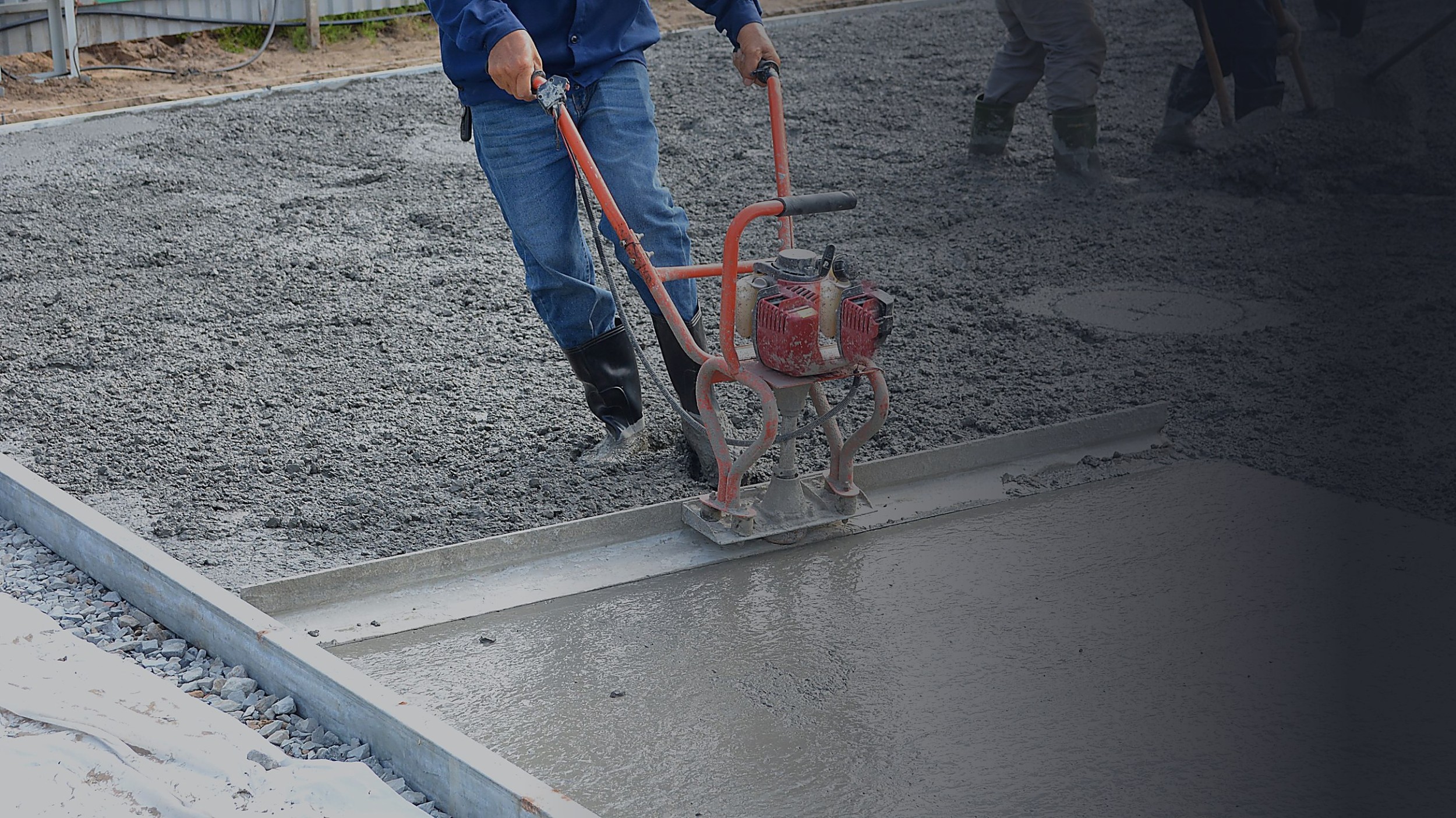Operário nivelando concreto fresco com régua vibratória